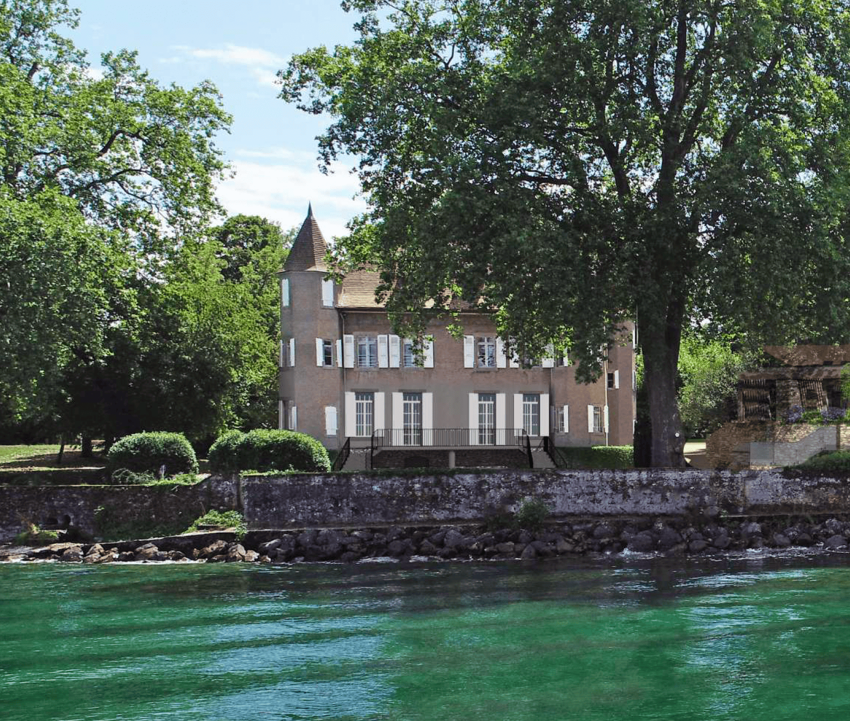 Château avec une tour, entouré d'arbres, au bord d'un lac à l'eau turquoise.