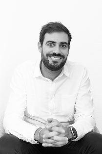 Portrait en noir et blanc d'un homme souriant en chemise blanche, les mains croisées.
