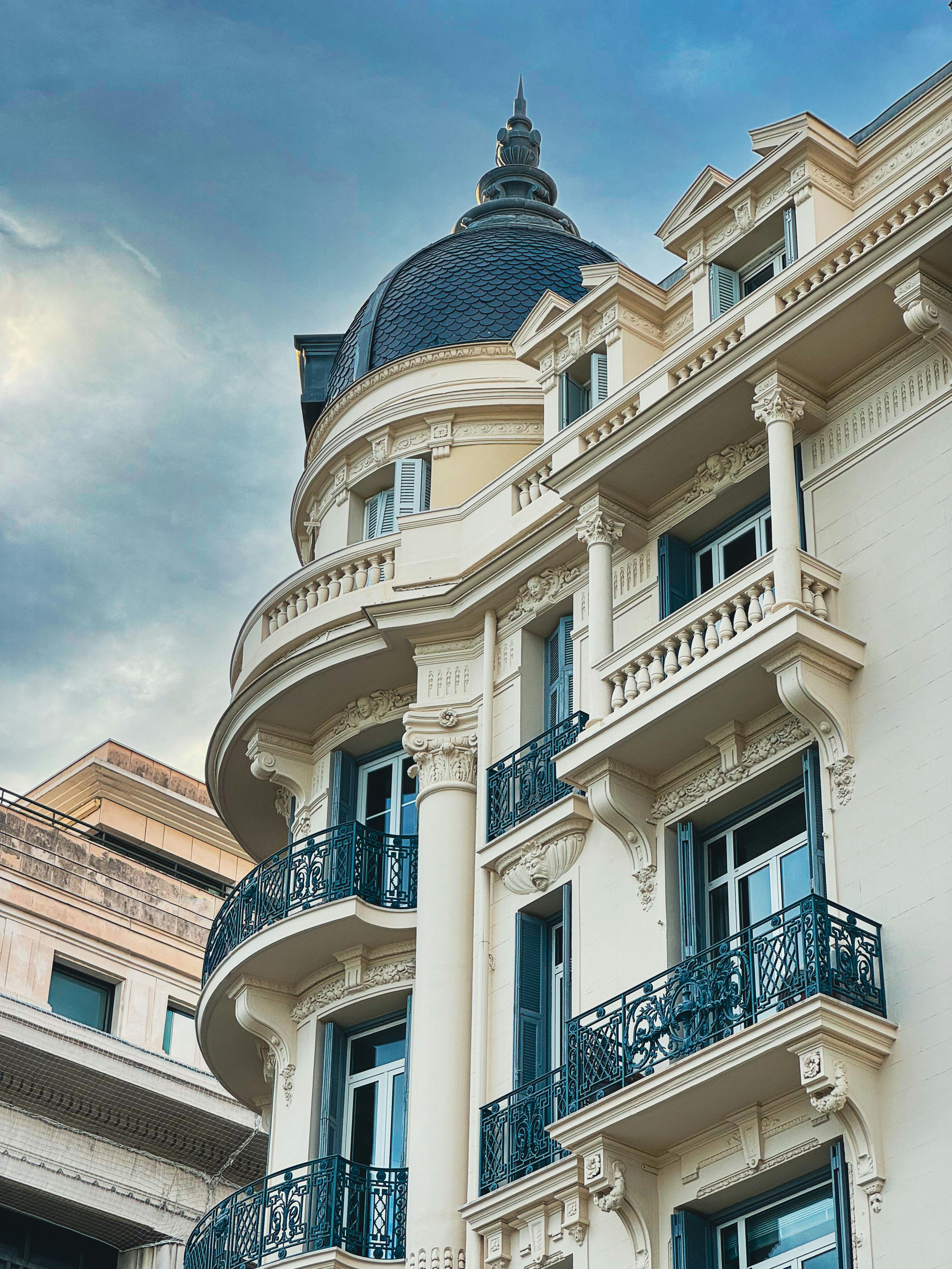Façade d'un bâtiment ancien avec balcons en fer forgé et un dôme orné sous un ciel nuageux.