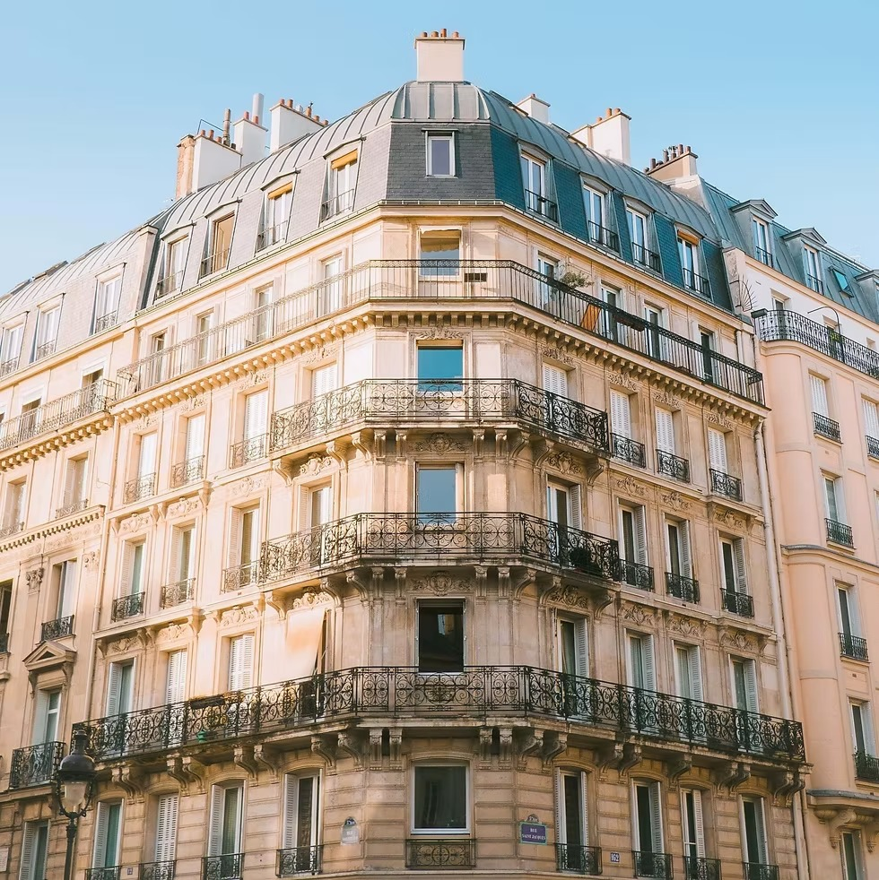Façade d'un bâtiment parisien avec balcons en fer forgé sous un ciel bleu clair.