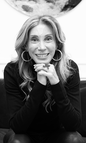 Femme souriante aux cheveux ondulés, posant les mains jointes sous le menton, en noir et blanc.