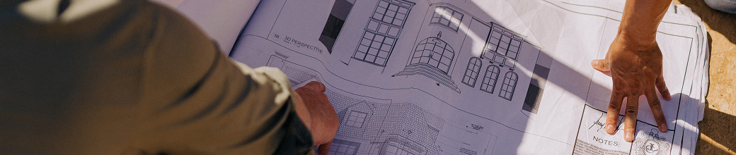 Hands pointing at architectural blueprints of a building with windows and a dome feature.