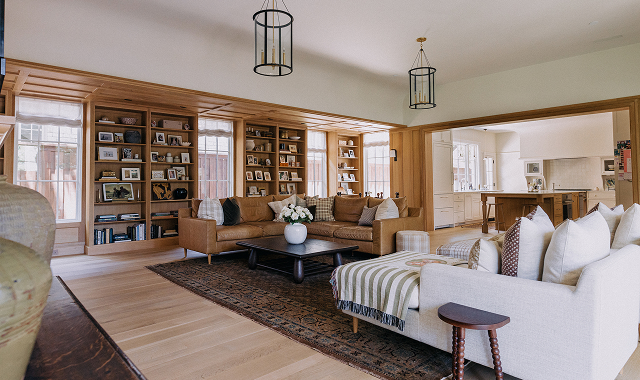 Spacious living room with brown sofa, white armchair, wooden bookshelves, and large windows.