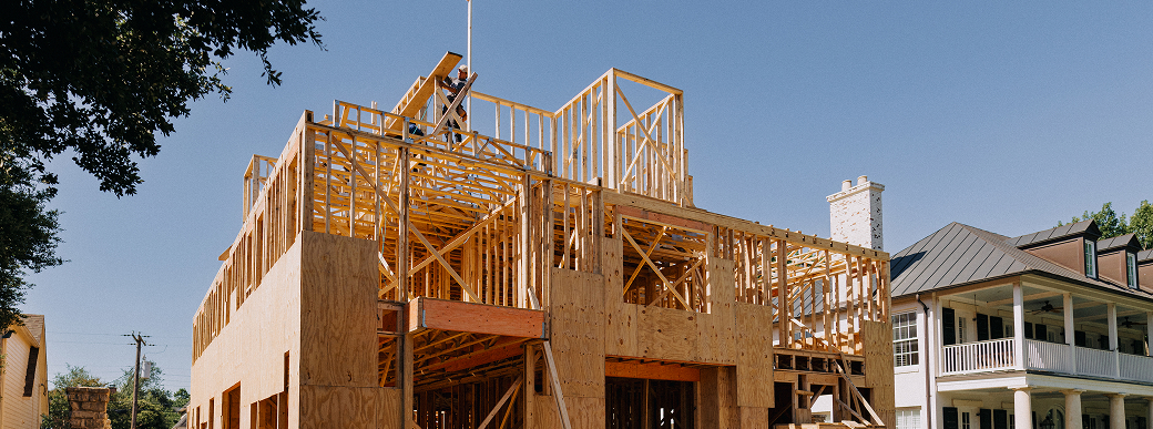 Wooden framework of a multi-story house under construction on a clear day.