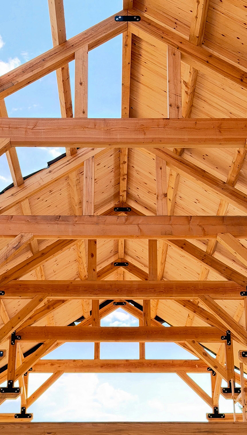 Wooden truss roof structure with light wood beams and blue sky visible through openings.