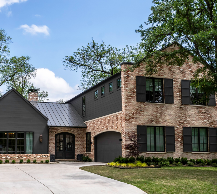 Modern two-story home with brick and dark siding, large windows, and a driveway under blue sky.