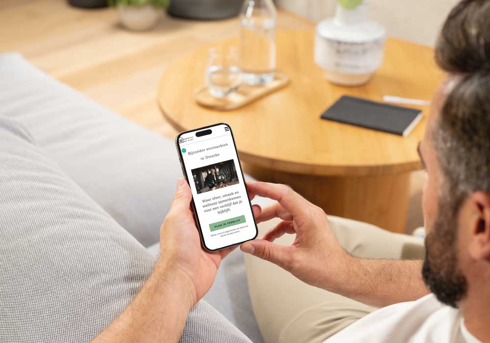 Een man zit op een bank en bekijkt een website over bijzondere overnachtingen op zijn telefoon.