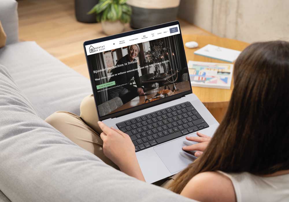 Vrouw op bank met een laptop waarop een website voor bijzondere overnachtingen in Drenthe te zien is.