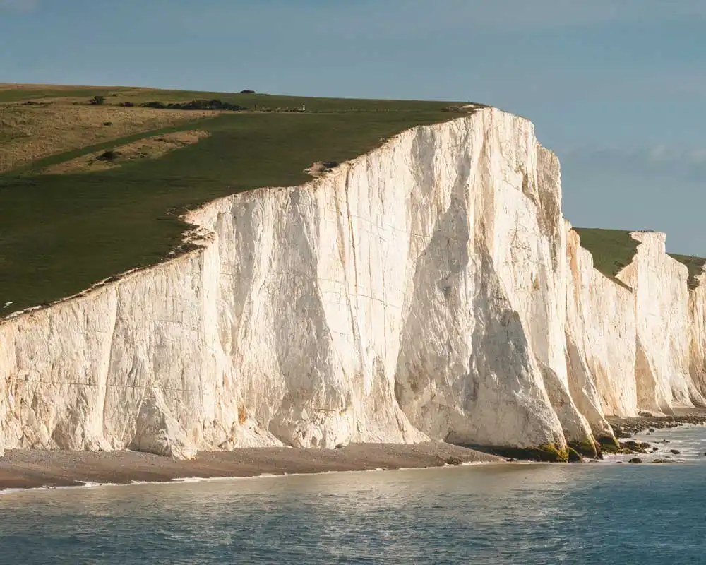 Seven Sisters white chalk cliffs above the sea, with green South Downs on the clifftop in Sussex