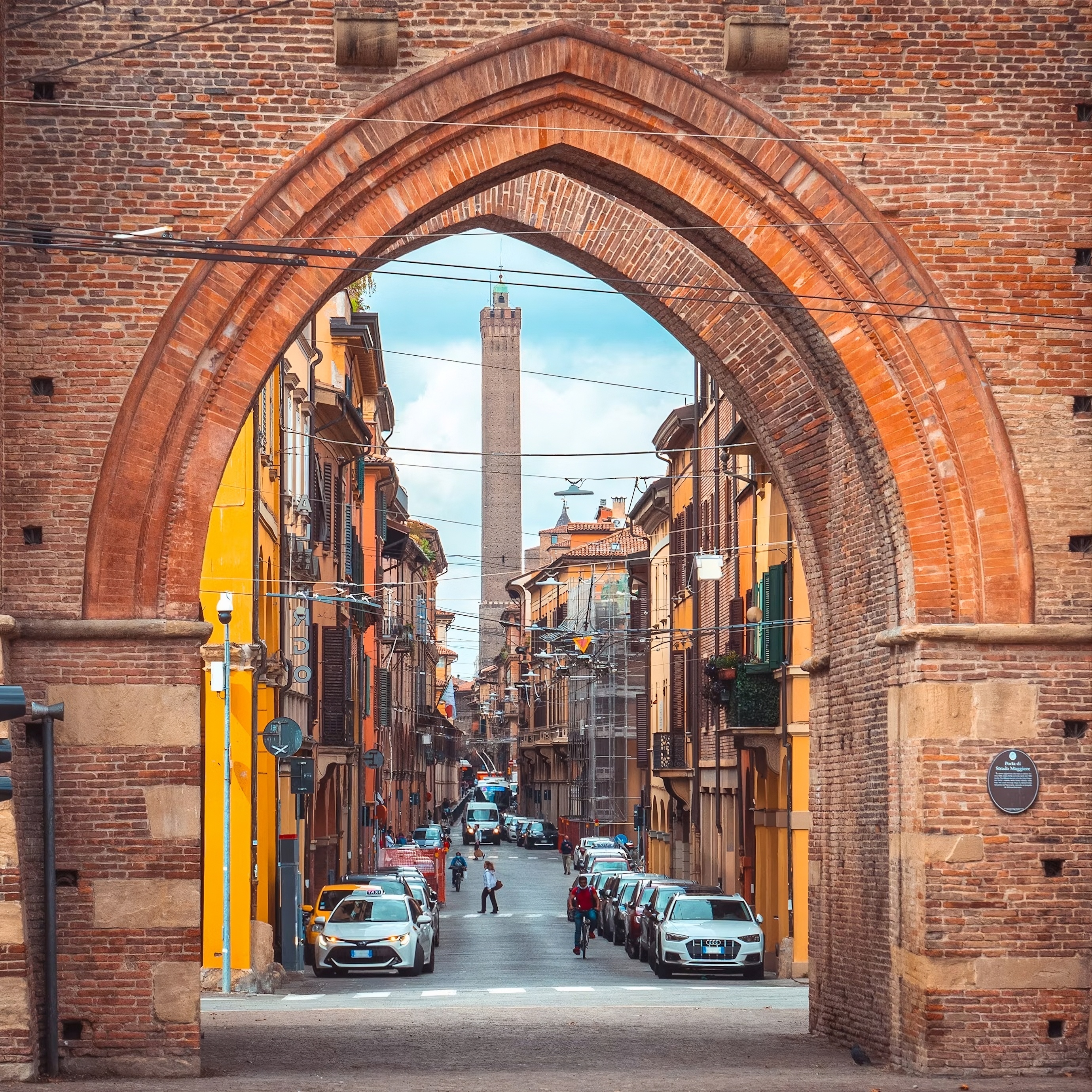 Scorcio di Bologna medievale con vista della Torre degli Asinelli attraverso un arco in mattoni.