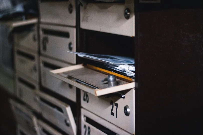 Courrier débordant d'une boîte aux lettres entrouverte dans un hall d'immeuble