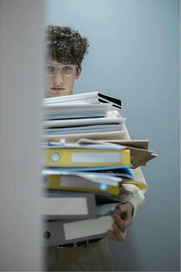 Collaborateur portant une pile instable de classeurs et de dossiers papier