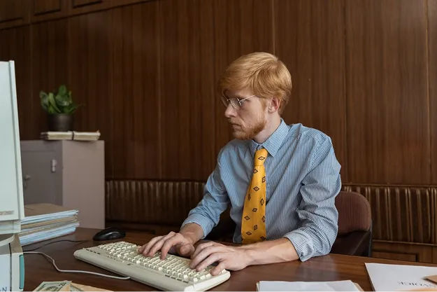 Employé de bureau en chemise et cravate saisissant des données sur un clavier d'ordinateur ancien