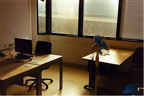 Bureau d'entreprise désert avec un poste informatique et un ventilateur devant une fenêtre