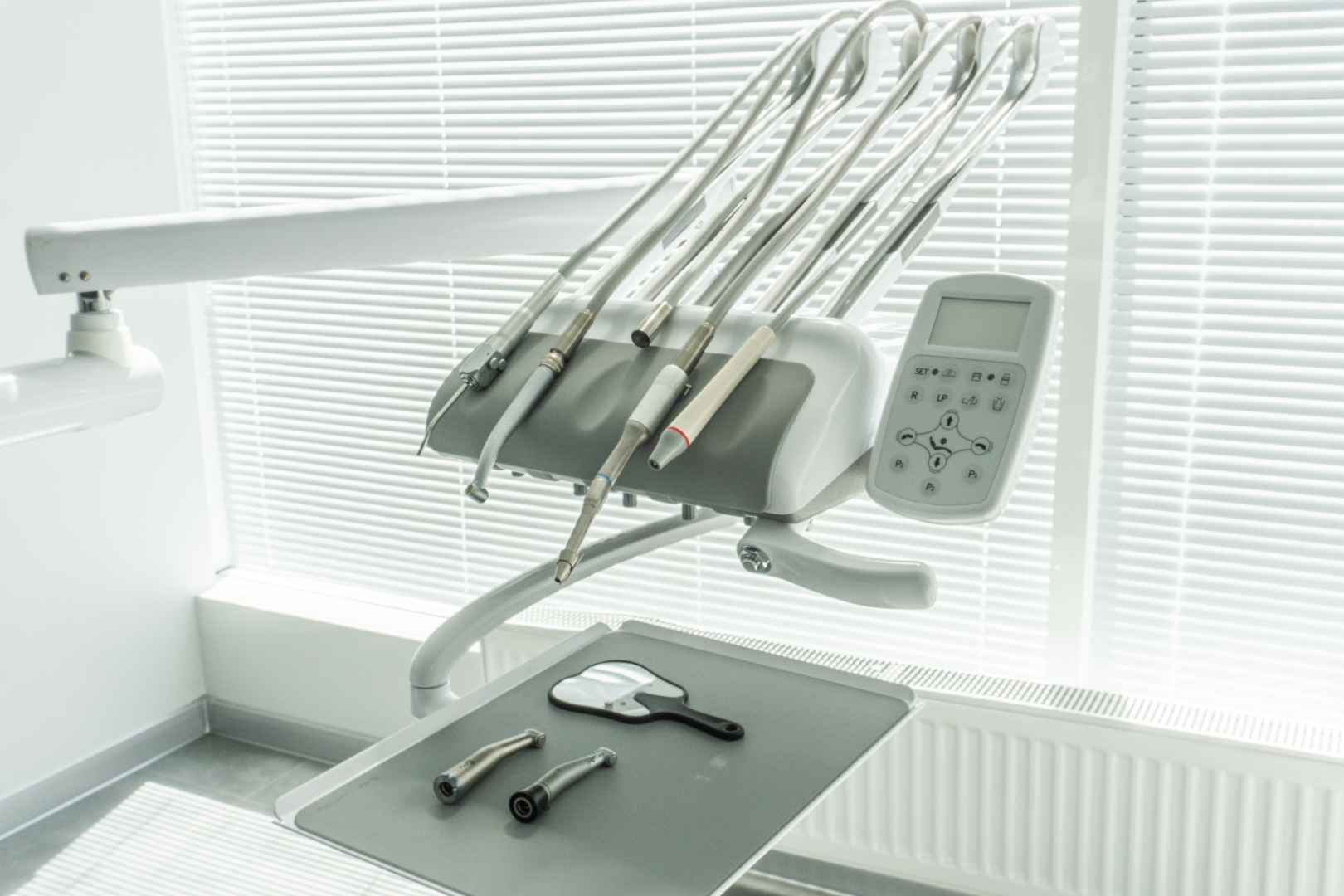 Dental instruments and tools arranged on a tray and holder in a bright dental clinic room.