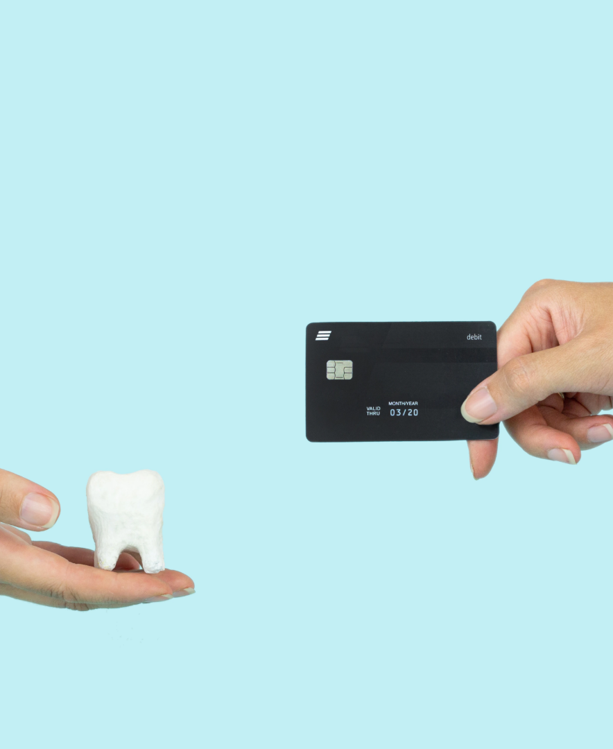 Hand holding a large tooth model and another hand holding a black debit card on light blue background.