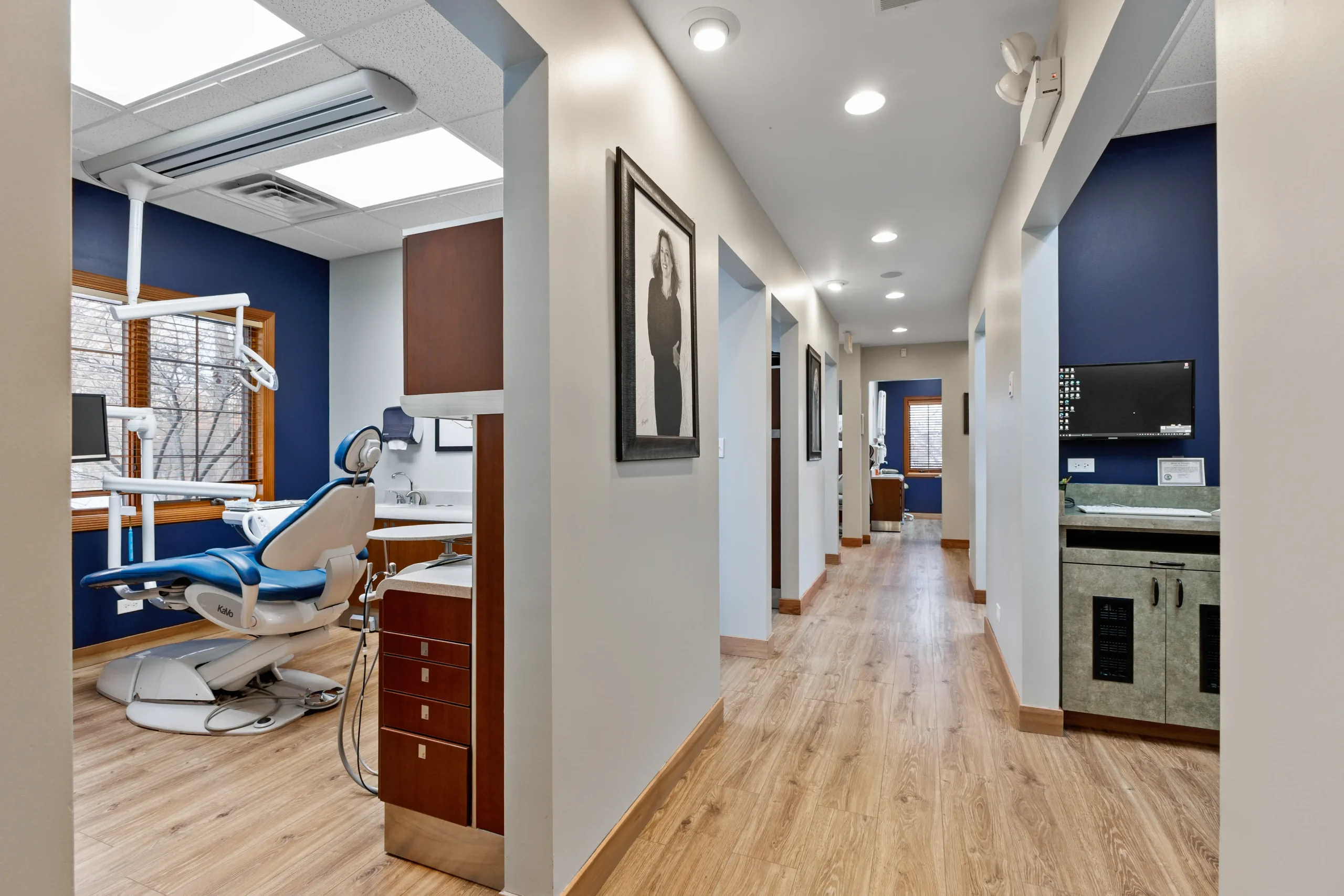 Hallway in a dental office with treatment rooms featuring blue dental chairs and wood flooring.
