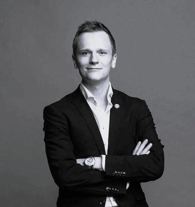 Hymyilevä mies puvussa kädet ristissä.