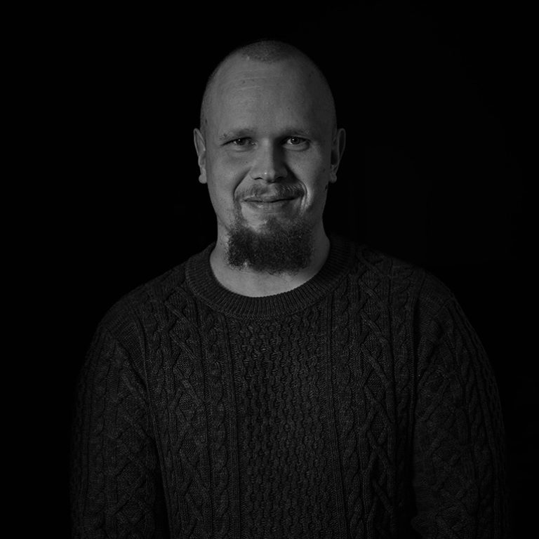 Mustavalkoinen muotokuva parrakkaasta, kaljusta miehestä, joka hymyilee ja katsoo kameraan.
