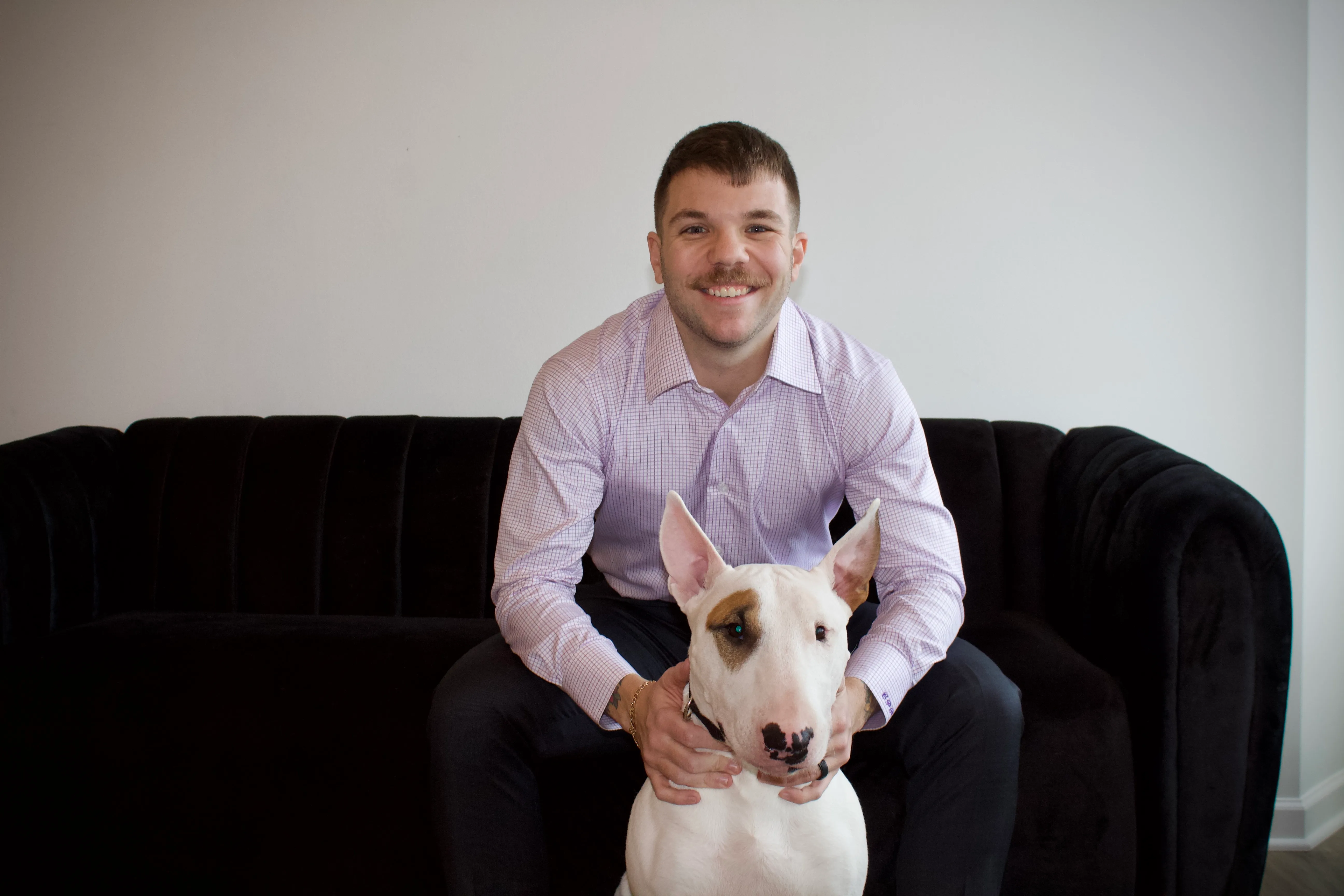 Collin sitting on a couch with Walter, a white bull terrier, on his lap