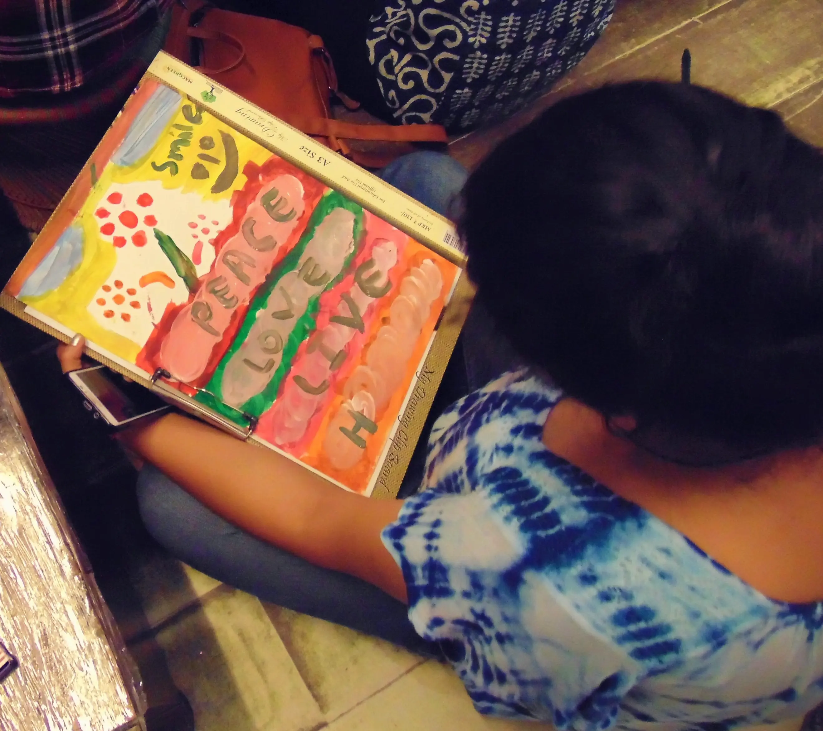 Person holding a colorful painting with words peace, love, hope, and a smiley face.