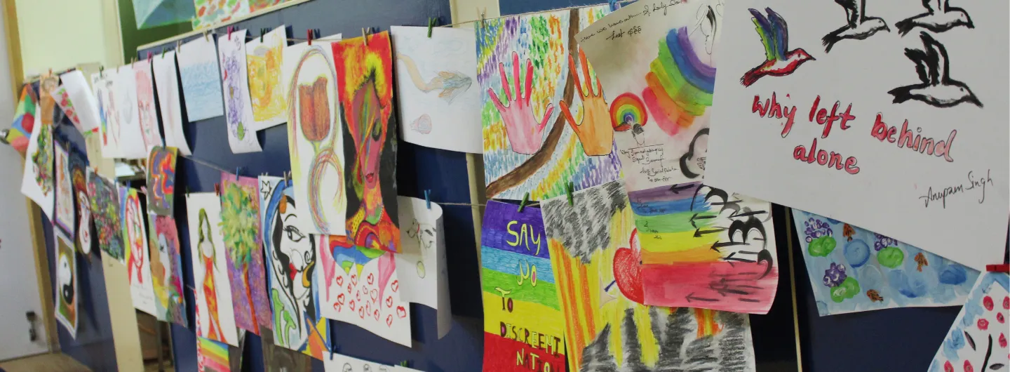 Colorful artworks and drawings hung on a wall, including rainbows, hands, birds, and flowers.