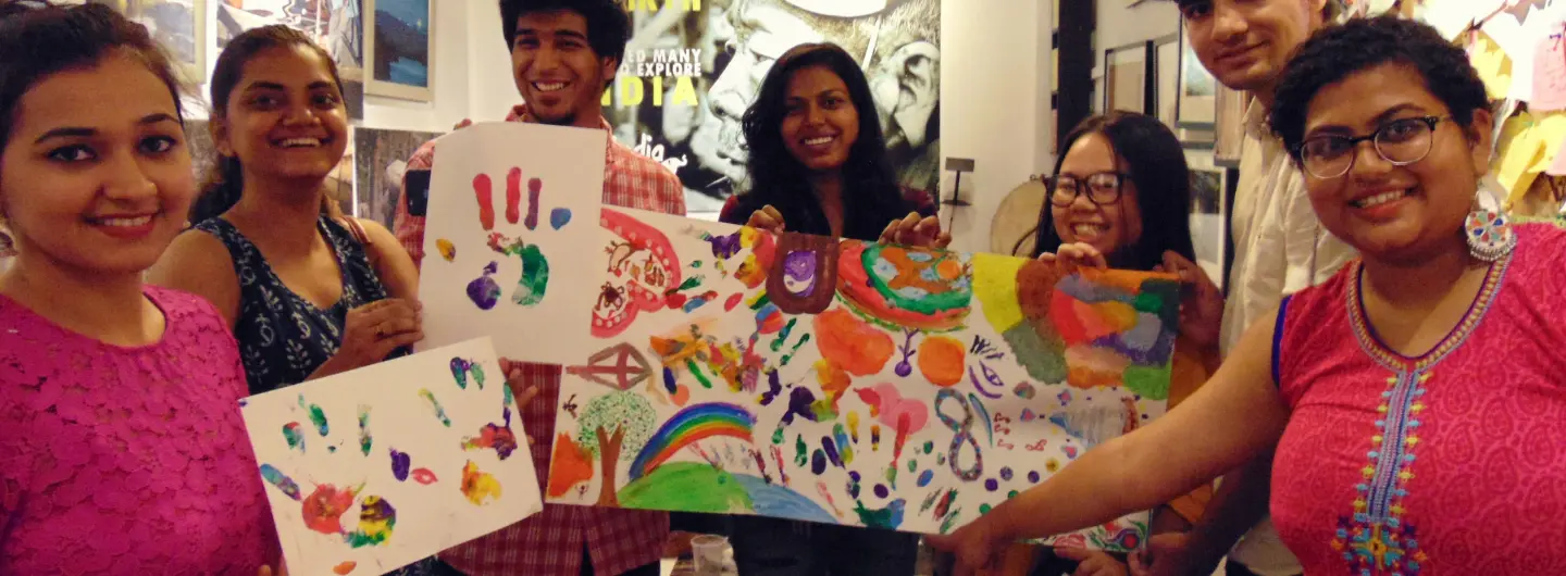 Group of seven people smiling and holding colorful handprint paintings on paper.