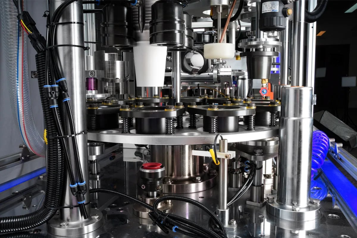 Close-up of complex stainless steel automated machinery with pipes, wires, and rotating parts.