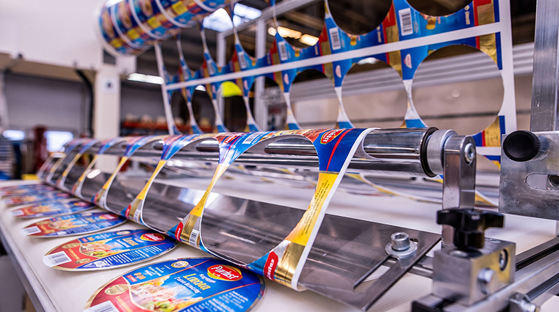 Machine rolling out printed packaging labels for food products in a production line.