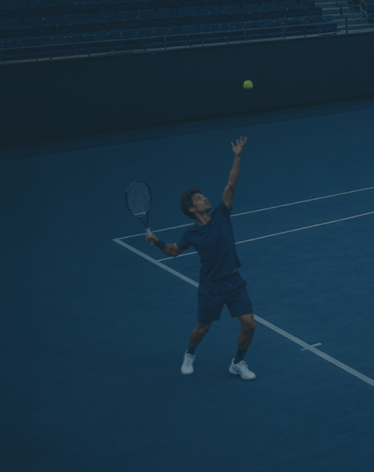 Male tennis player wearing blue prepares to serve on an empty blue tennis court.