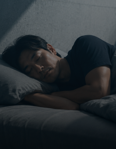 Man sleeping on gray pillow and bed with a dark shirt in a dimly lit room.