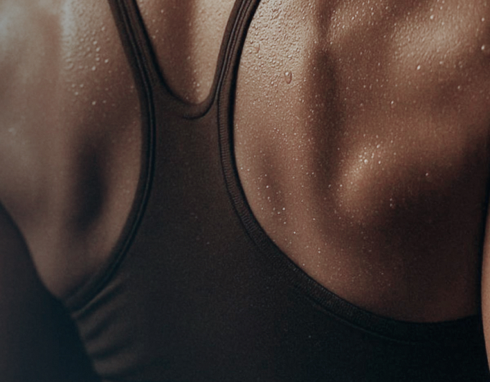 Close-up of a person's sweaty back wearing a black tank top, highlighting skin texture and water droplets.