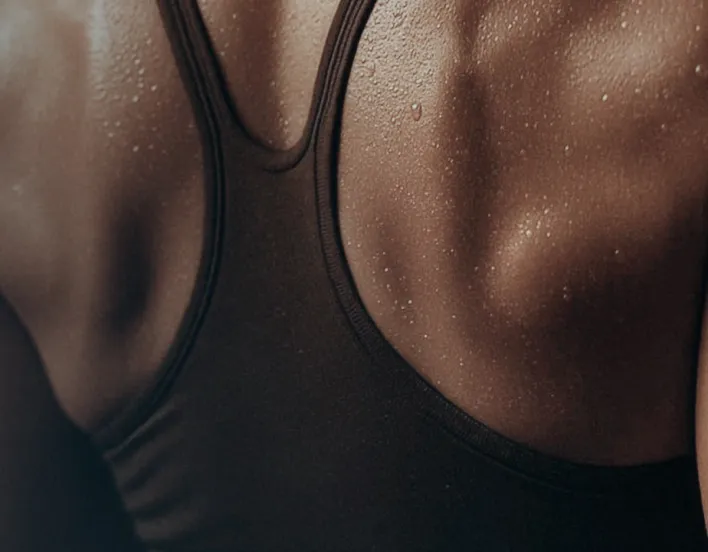 Close-up of a person's sweaty back wearing a black tank top, highlighting skin texture and water droplets.
