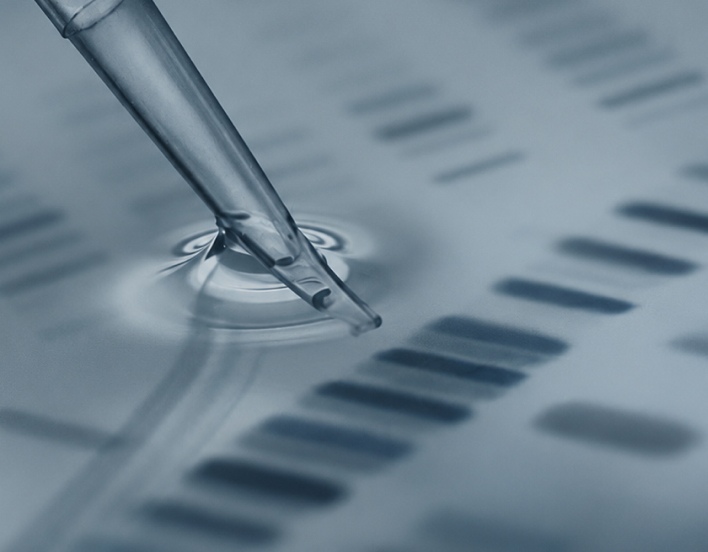 Close-up of a pipette dispensing liquid onto a sheet with DNA bands pattern in a lab setting.