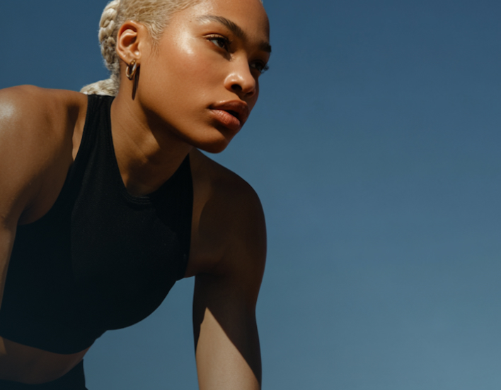 Focused woman in black sportswear outdoors with braided hair against clear blue sky.