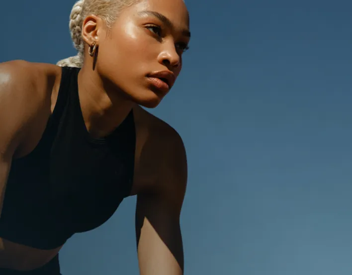 Focused woman in black sportswear outdoors with braided hair against clear blue sky.