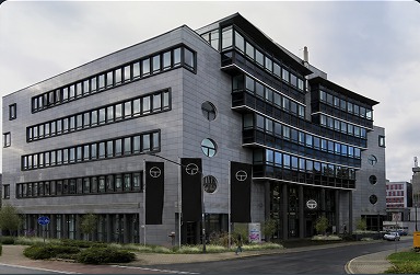 Modern multi-story office building with many windows and round window accents on a cloudy day.