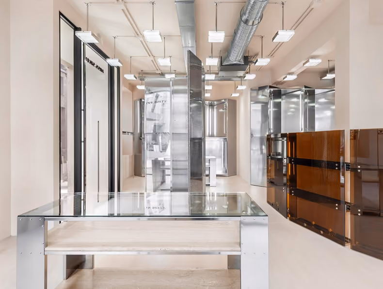 Modern interior with metal and glass tables, metal partitions, and industrial ceiling lights.