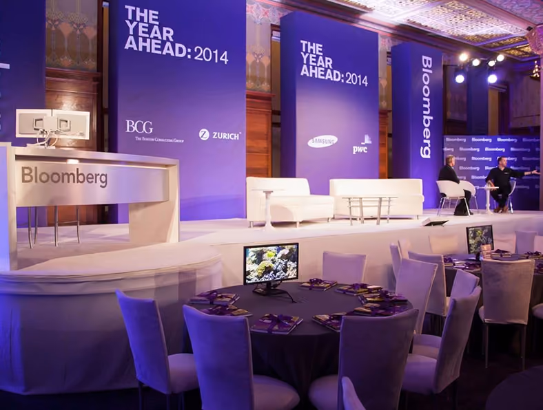 Conference stage with Bloomberg branding and 'The Year Ahead: 2014' banners with seated hosts on stage.