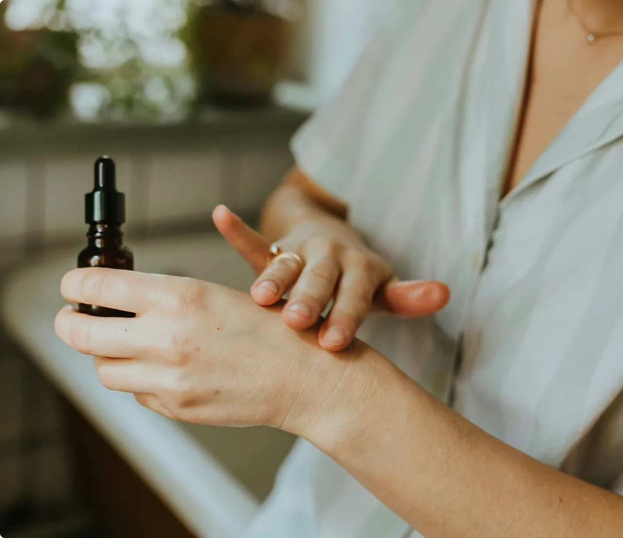 Person applying skincare serum from a dropper bottle onto the back of their hand.