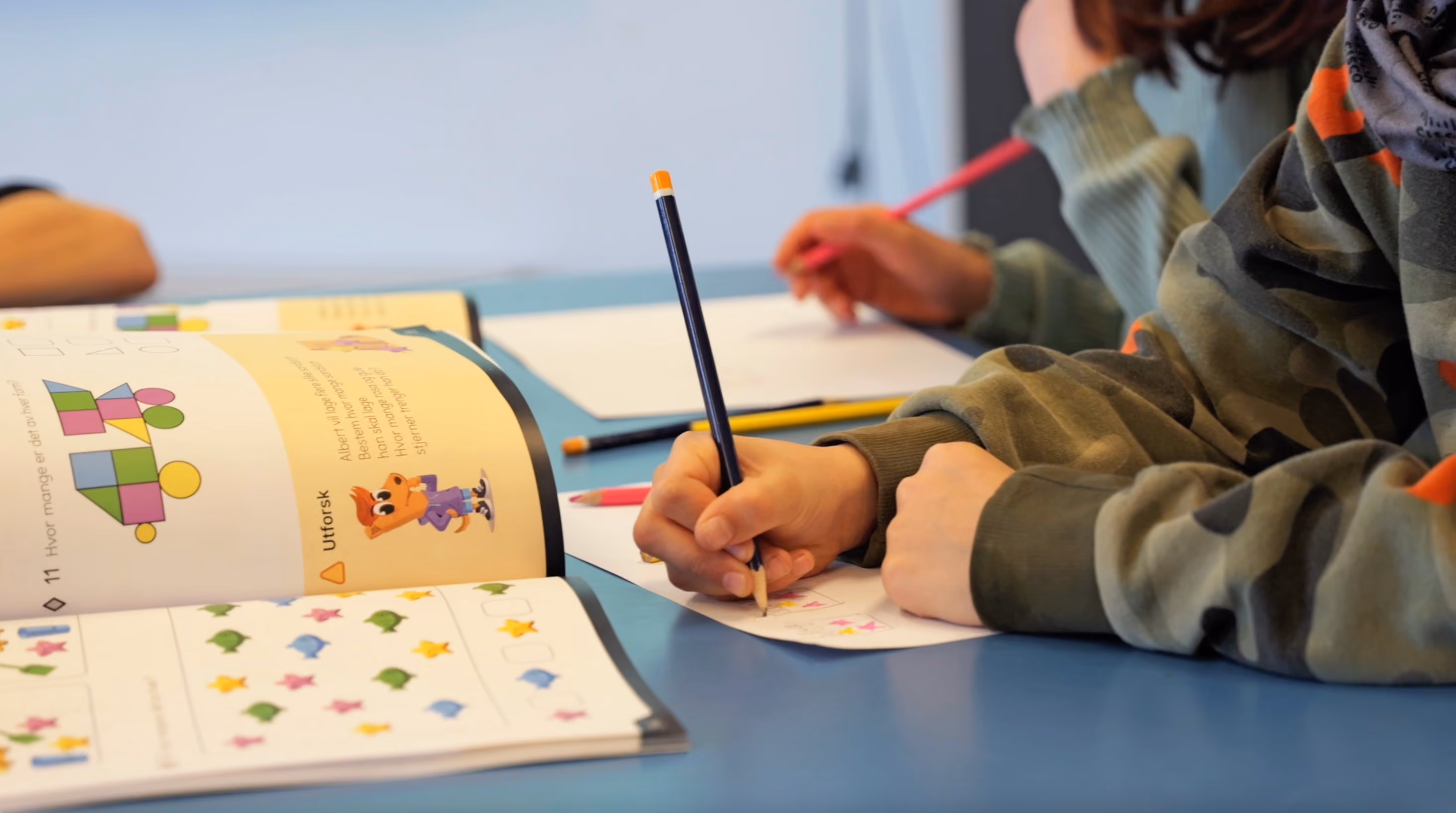 To elever sitter og jobber med utforskende oppgaver i arbeidsbøkene.