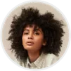 Portrait of a young woman with curly dark hair wearing a light-colored shirt, looking slightly upward with a neutral expression.