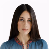 Portrait of a woman with long straight dark brown hair wearing a blue top with a decorative red and pink neckline on a white background.