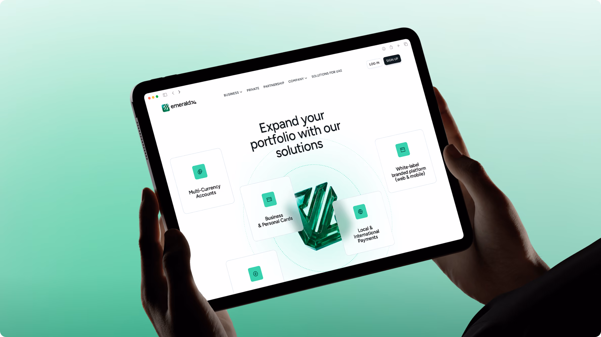 Person holding a tablet displaying a website for Emerald24 with the header "Expand your portfolio with our solutions" and options including Multi Currency Accounts, Business & Personal Cards, Local & International Payments, and White-label branded platform.