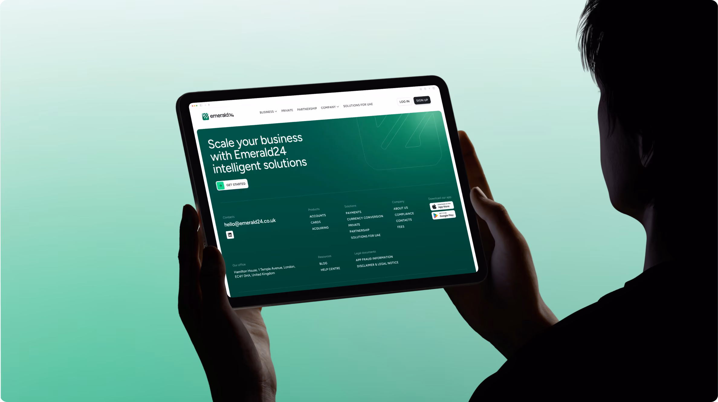 Person holding a tablet displaying Emerald24 website with the text 'Scale your business with Emerald24 intelligent solutions' on a green gradient background.