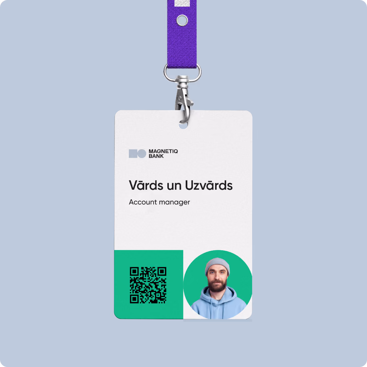Employee ID badge for MAGNETIQ BANK with placeholder text 'Vārds un Uzvārds' and title 'Account manager', featuring a QR code and a circular photo of a man with a beard wearing a gray beanie and blue hoodie, attached to a purple lanyard.