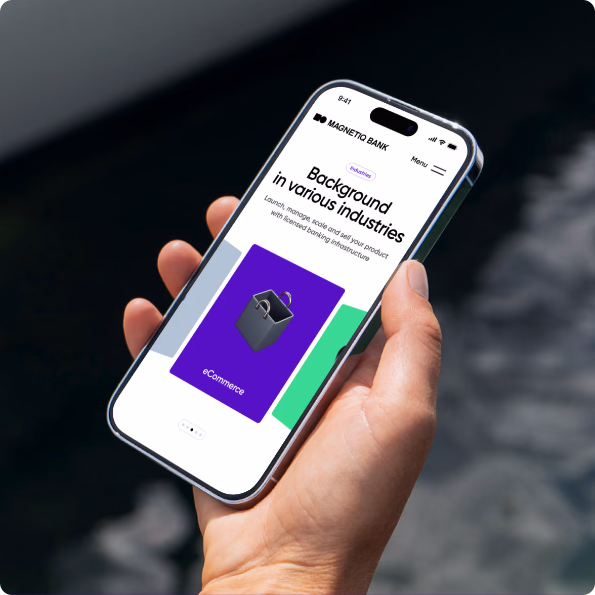 Hand holding a smartphone displaying a webpage for Magnetiq Bank with the headline 'Background in various industries' and a section highlighting eCommerce with a shopping bag icon.