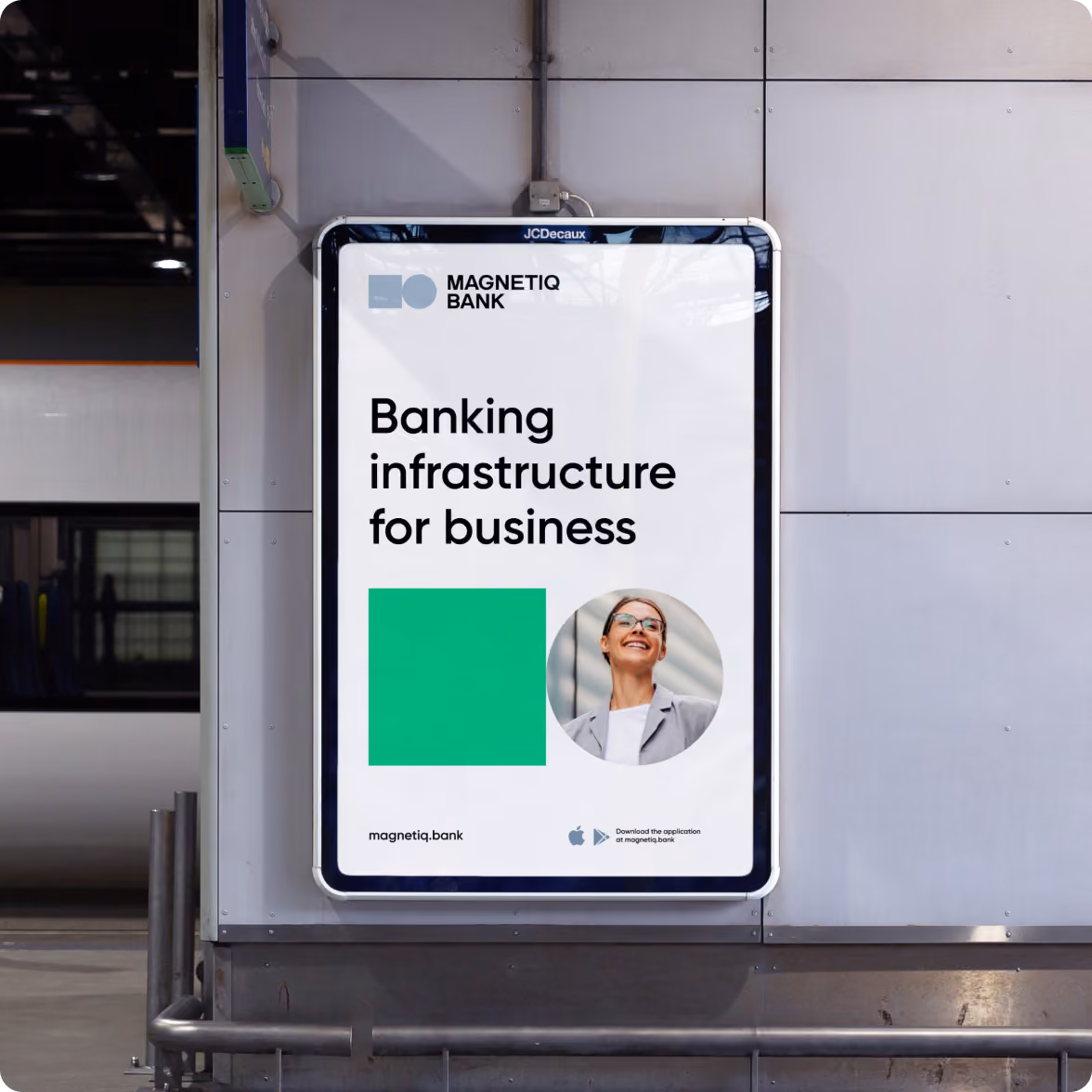 Outdoor advertisement board for Magnetiq Bank displaying the text 'Banking infrastructure for business' with the bank's logo, a green square, and a circular photo of a smiling woman wearing glasses and a gray blazer, with download icons for app stores at the bottom.