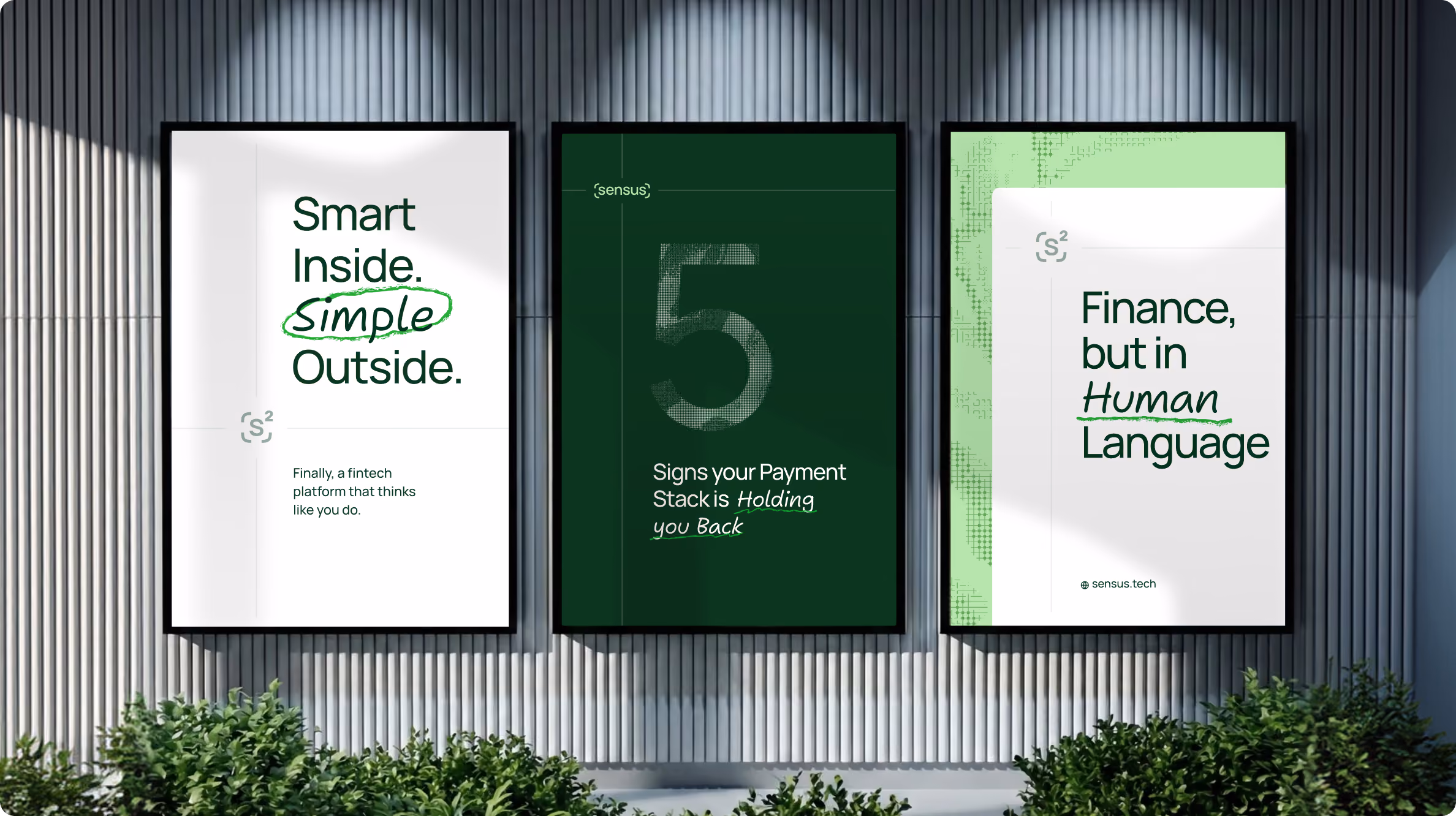 Three framed posters on a corrugated gray wall above green shrubs: left poster says 'Smart Inside. simple Outside.' with 'simple' circled and smaller text 'Finally, a fintech platform that thinks like you do.'; middle poster has a large number 5 and text 'Signs your Payment Stack is Holding you Back'; right poster says 'Finance, but in Human Language' with 'Human' underlined and small text 'sensus.tech'.