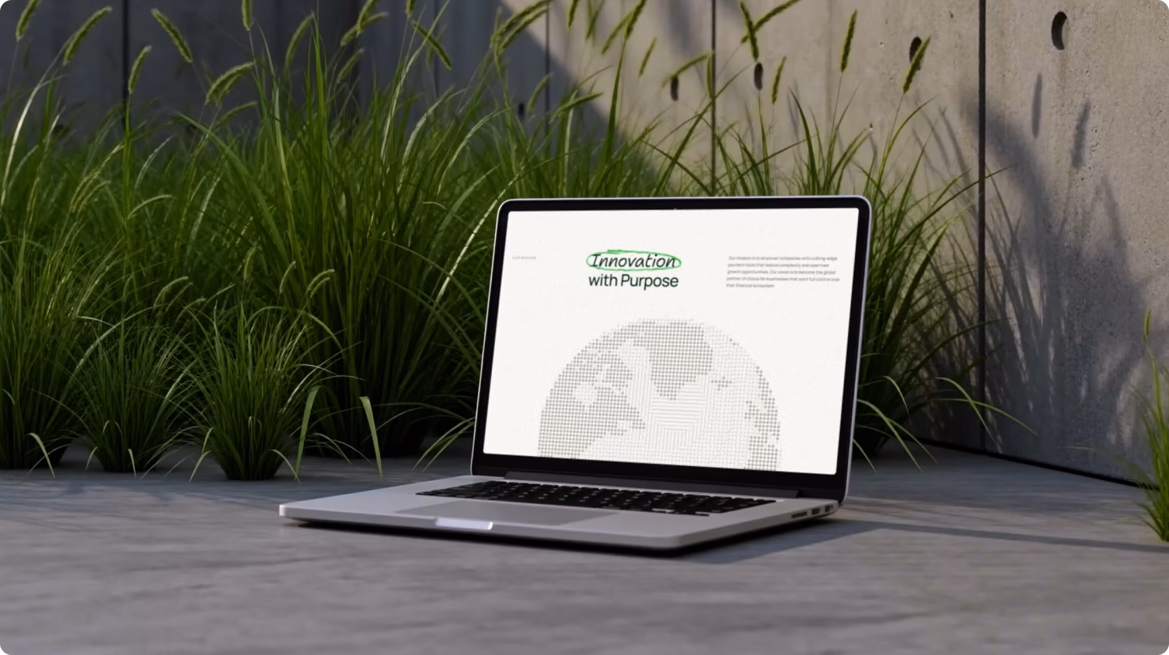 Open laptop placed on a concrete surface outdoors with tall green grass in the background and a concrete wall; the screen shows text reading 'Innovation with Purpose' above a dotted globe illustration.